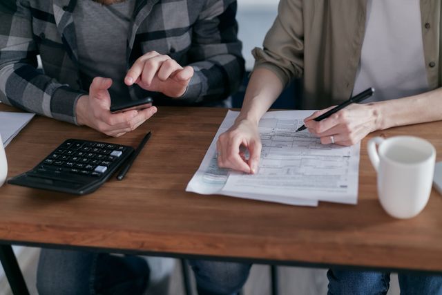 Two people reviewing paperwork and using a calculator at a table 